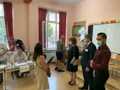 Избирателна секция в класна стая: членове на комисия на маса, избиратели и наблюдатели с маски